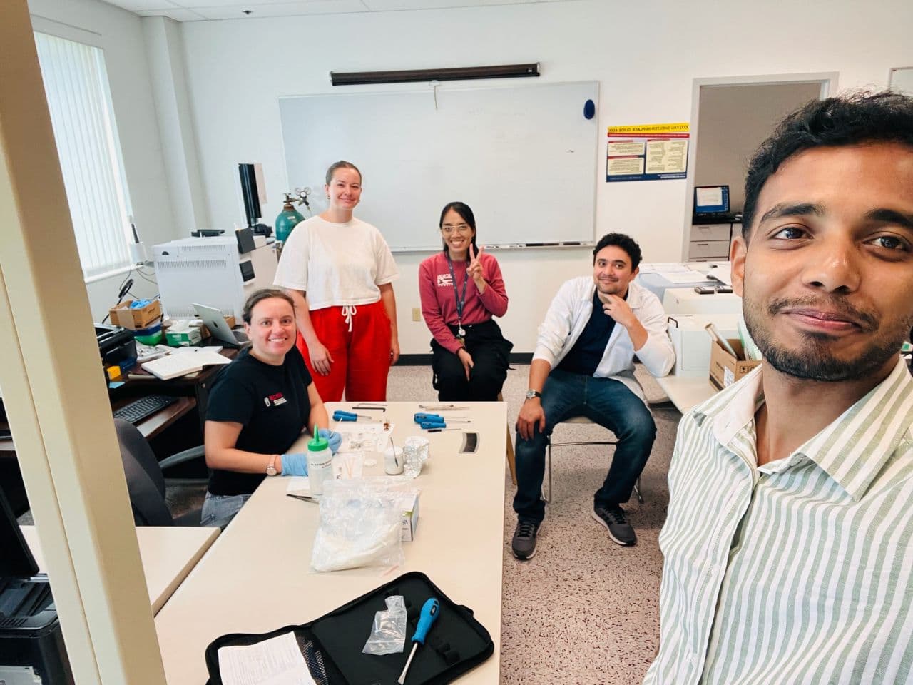 Transform Lab members taking a group selfie around the lab worktable during GC ion source cleaning